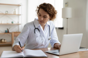 Serious female doctor working using laptop and writing notes